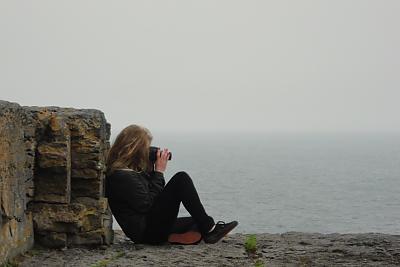 Student taking picture while sitting at the edge of the Cliffs of Moher